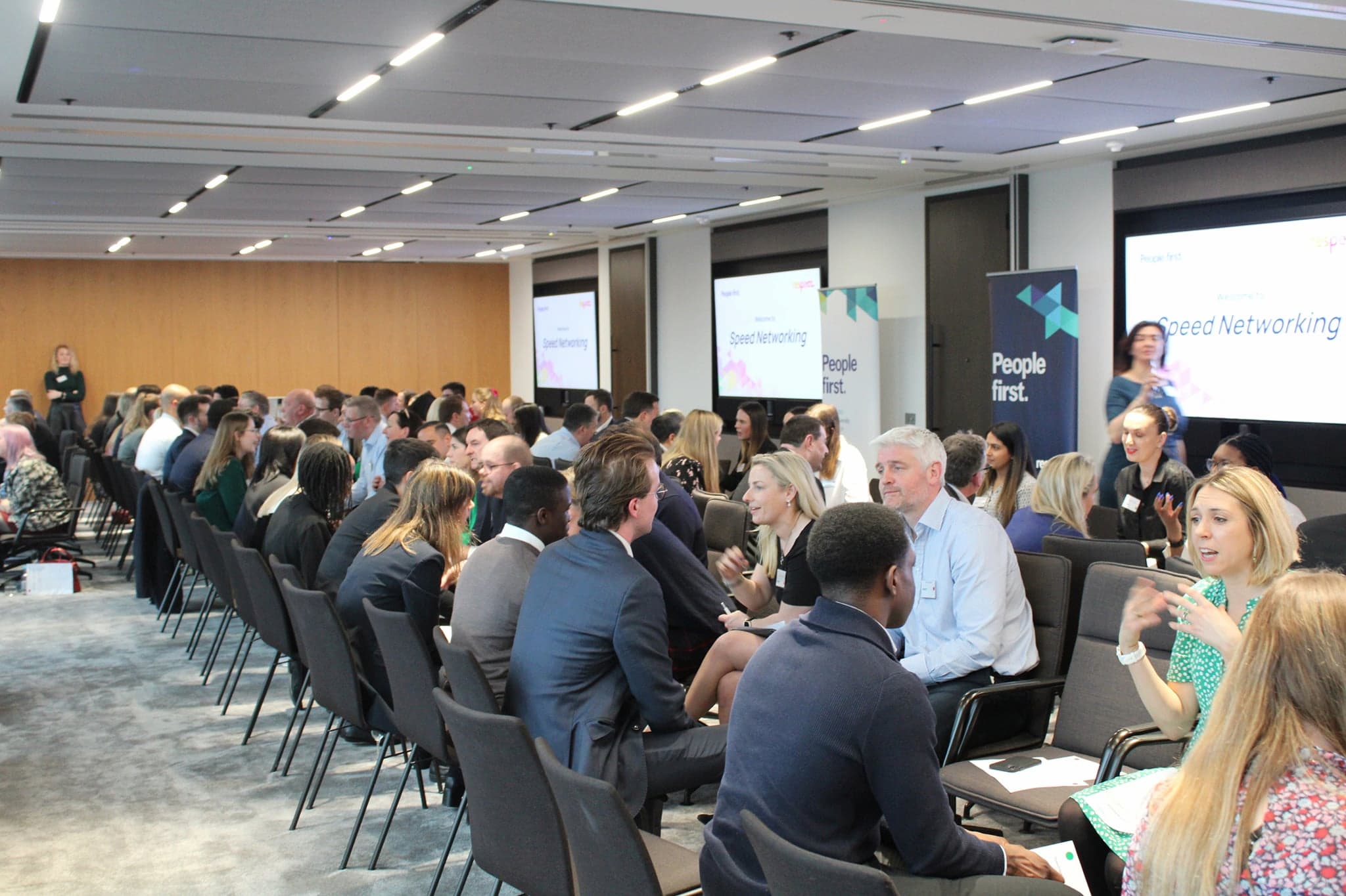 Speed networking in progress. Rows of pairs of people in chairs, talking. 